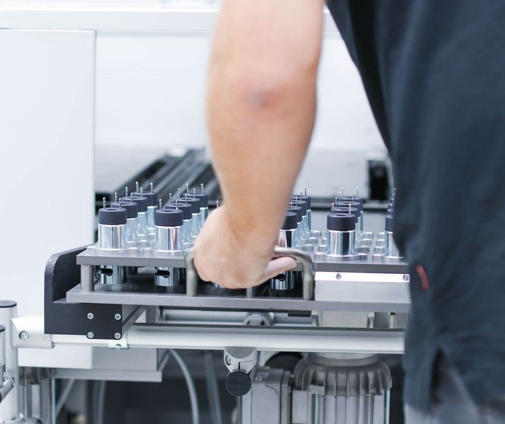Ein Mitarbeiter schiebt Elektromagnete in die Vergussanlange in der Montage bei Magnetbau Schramme